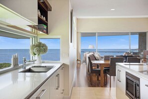 Eine moderne Küche mit Meerblick, ein Essbereich mit Tisch und Stühlen sowie ein großes Fenster.