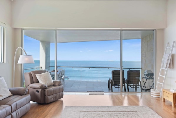 Ein modernes Wohnzimmer mit Meerblick, einem Balkon mit Sitzgelegenheit und einem großen Fenster.
