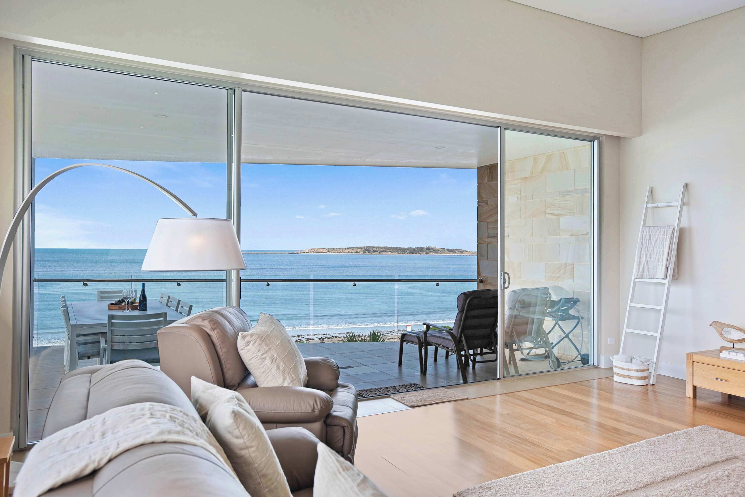 A modern living room with a large sliding glass door leading to a balcony with a view of the sea.