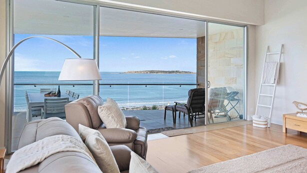 Una sala moderna con un gran ventanal corredero que da a un balcón con vista al mar.