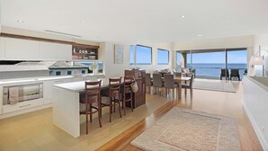 Una cocina moderna con una isla central, comedor con sillas y grandes ventanales con vistas al mar.