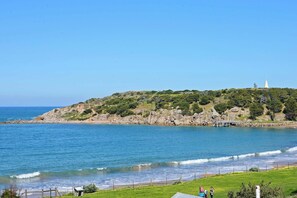 Eine Küstenlandschaft mit einem grasbewachsen Hügel, einem Leuchtturm und einem Strand.