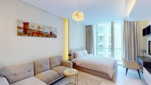 Ein modernes Hotelzimmer mit einem Bett, einer Couch, einem kleinen Tisch, einem Gemälde und einem großen Fenster mit Vorhängen.