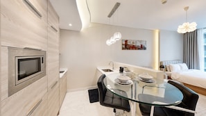 A modern hotel room with a kitchenette, a glass dining table, a bed, and a painting on the wall. - Elegant Studio in Bahrain Bay in Waterbay (Manama)