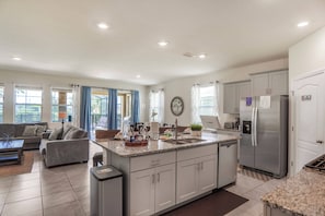 A modern kitchen with a central island, stainless steel appliances, and a dining area with a sofa and coffee table. - 6BR Pool Home Near Disney at Solterra (Davenport)