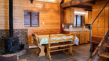A cozy cabin interior with a wooden bench, a fireplace, a kitchen area, and a staircase.
