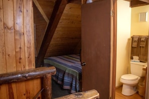 A wooden interior with a sloped ceiling, a bed with a striped blanket, and a white toilet. - Duplex Cabin with Spacious Interior Great for Groups in Arizona (Flagstaff)