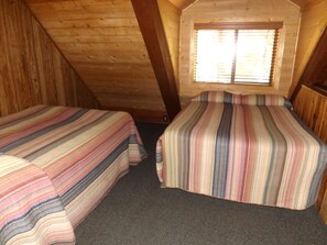 A small, cozy attic bedroom with two beds, a sloped ceiling, and a window with blinds. - Duplex Cabin with Spacious Interior Great for Groups in Arizona (Flagstaff)