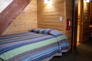 A single bed with a striped blanket in a wooden room with a sloped ceiling and a fire extinguisher mounted on the wall. - Duplex Cabin with Spacious Interior Great for Groups in Arizona (Flagstaff)