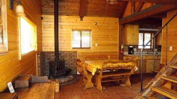 L’intérieur d’un chalet en bois comprend une table à manger, des bancs, une cheminée et un coin cuisine.