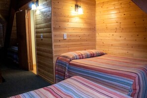 Una habitación acogedora con paredes de madera, una cama con manta a rayas y una lámpara sobre la cama.