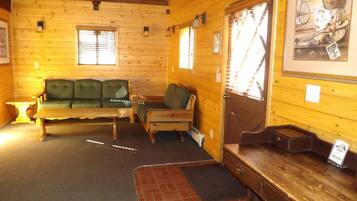 L’intérieur d’un chalet en bois, avec un canapé, un banc, une petite table et un tableau encadré accroché au mur.