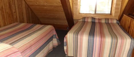 Ein kleines, gemütliches Schlafzimmer im Dachgeschoss mit zwei Betten, geneigter Decke und einem Fenster mit Jalousien.