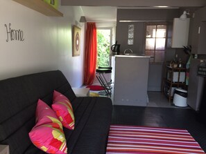 A compact living space with a sofa, a kitchen area, and a dining table. - Furnished studio with a private terrace, in a quiet, green setting 10 minutes from the sea (Lattes)