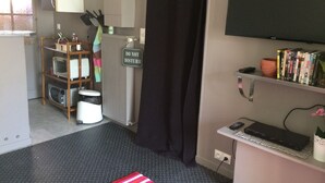 Quarto de hotel compacto com cozinha compacta, televisão, estante e um aviso 'Não Perturbe'.