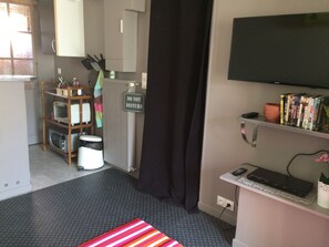 Ein kompaktes Hotelzimmer mit Küchenzeile, Fernseher, Bücherregal und einem 'Bitte nicht stören'-Schild.