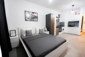 A modern bedroom with a bed, bedside tables, a wardrobe, and a kitchenette. - Klea's Downtown City Apartment Suite (Larnaca)