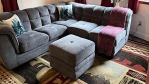 En sektionssoffa med en tillhörande pall, en mönstrad matta och en inramad tavla på väggen.