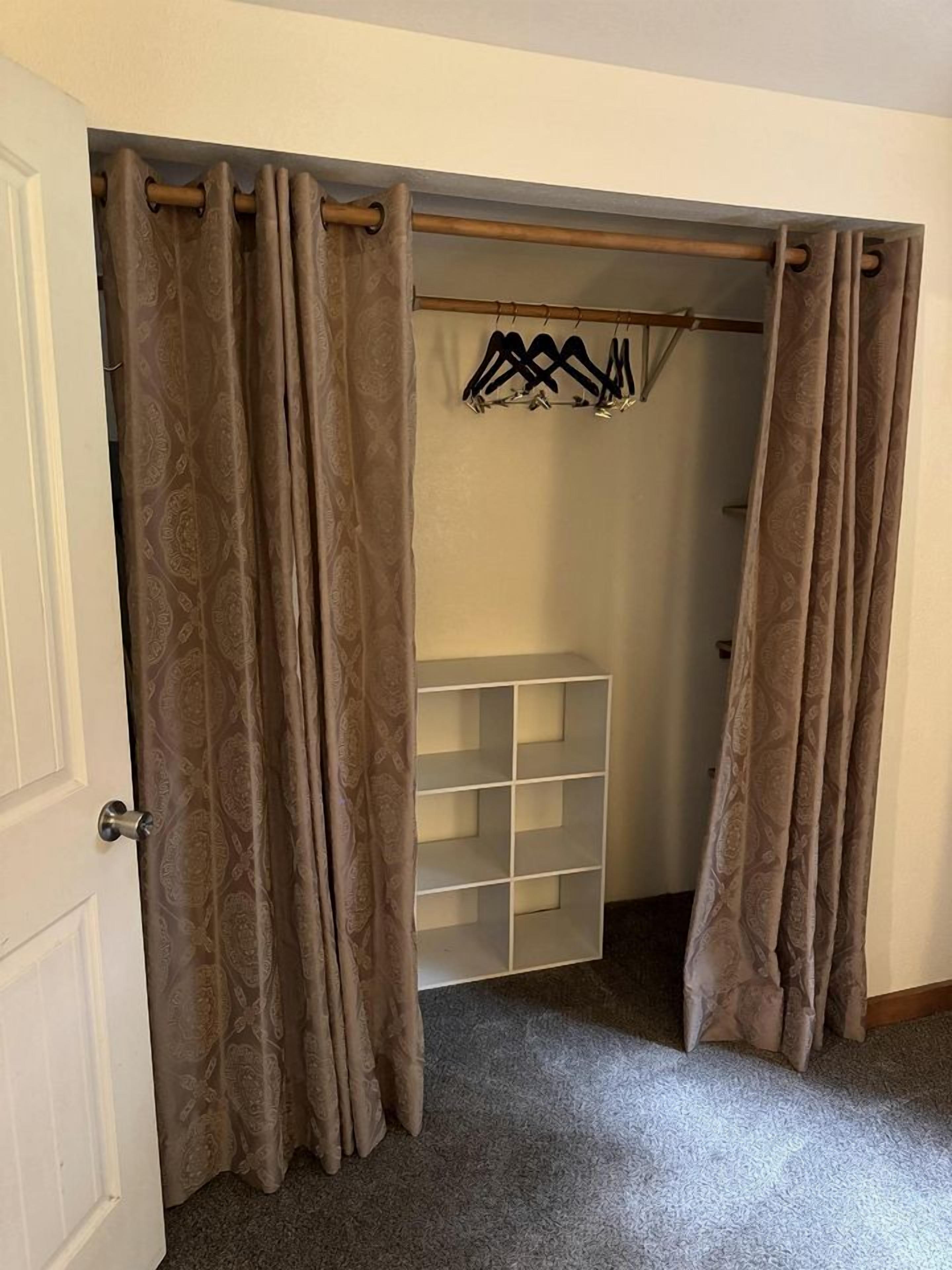 A walk-in closet with a hanging rod, shelves, and a door with curtains.