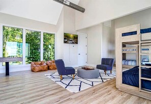 Ein modernes Zimmer mit Holzboden, einer Couch, einem Couchtisch, einem Etagenbett und großen Fenstern mit Blick auf Grünflächen.
