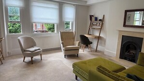 A room with a fireplace, a green sofa, a beige armchair, and a wooden bookshelf. - Light, airy, great location, newly decorated and furnished. Great views. (London)