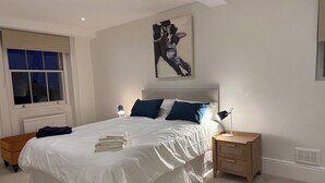 A bedroom with a large bed, bedside tables, a window, and a wall-mounted artwork. - Light, airy, great location, newly decorated and furnished. Great views. (London)