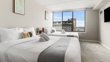 A hotel room with two beds, a large window with a city view, a flat-screen TV, and a ceiling with a speckled pattern.