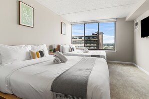 Habitación de hotel con dos camas, un ventanal con vistas a la ciudad, un televisor de pantalla plana y un techo con diseño moteado.
