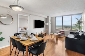 Una sala de estar moderna con comedor, televisor de pantalla plana y un ventanal con vistas a la ciudad.