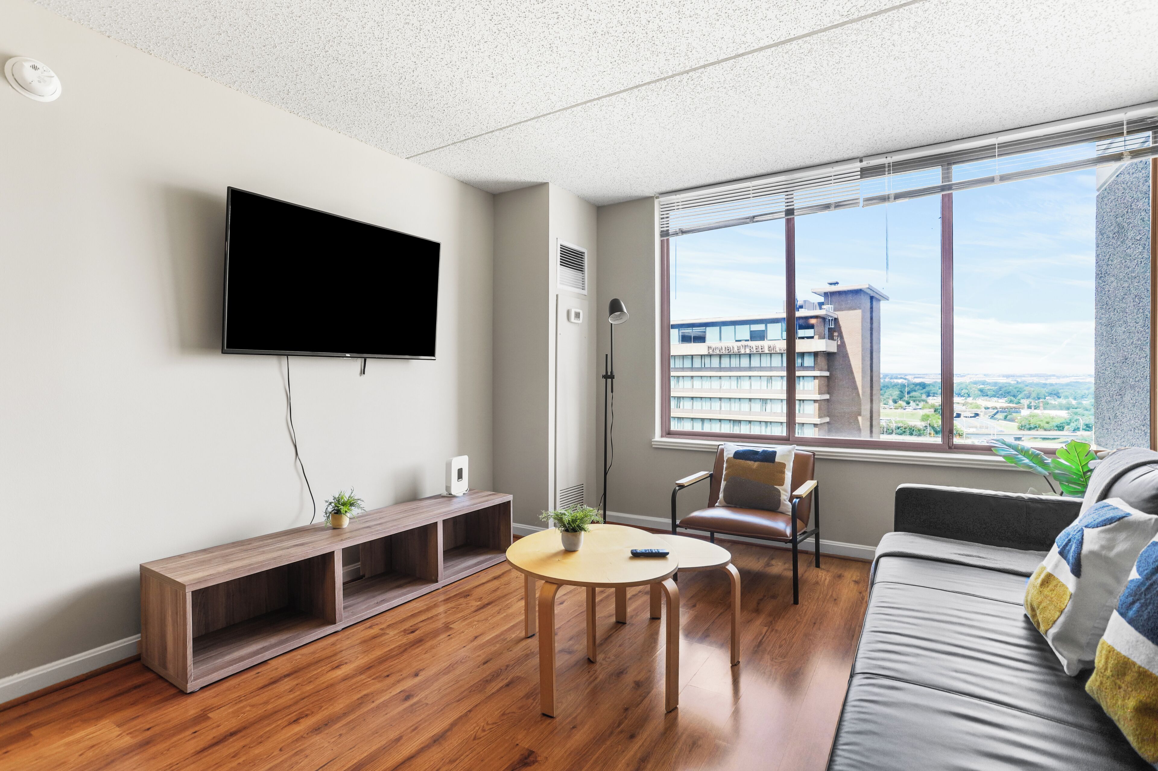 Een moderne woonkamer met een flatscreen televisie, een ronde salontafel, een bank en een raam met uitzicht op de stad.