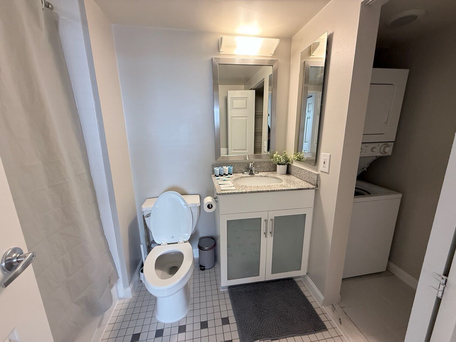 A bathroom with a toilet, sink, mirror, and a washing machine in the corner.