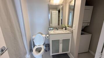 A bathroom with a toilet, sink, mirror, and a washing machine in the corner.