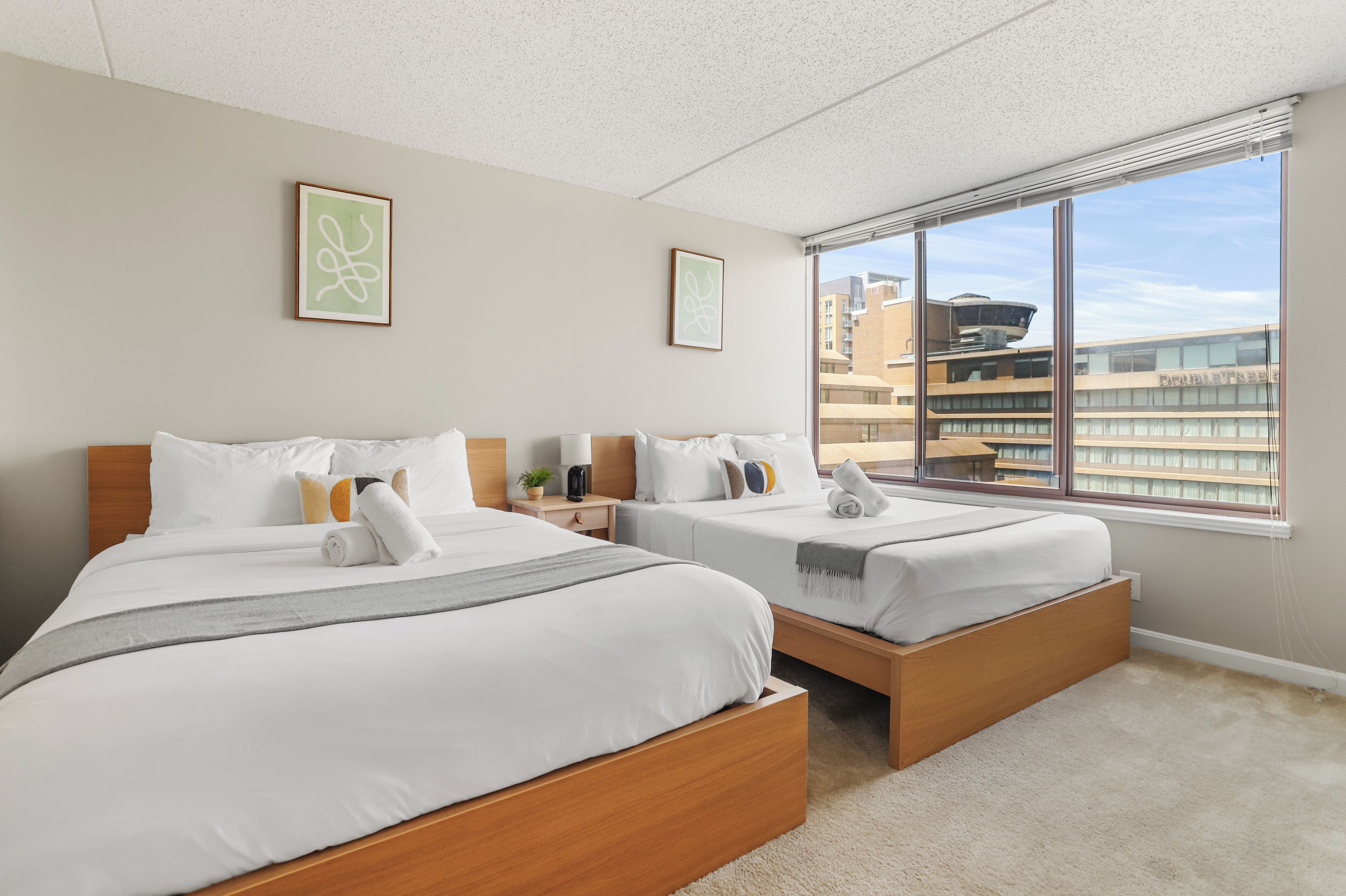 Habitación de hotel con dos camas, un ventanal grande y vistas a la ciudad.