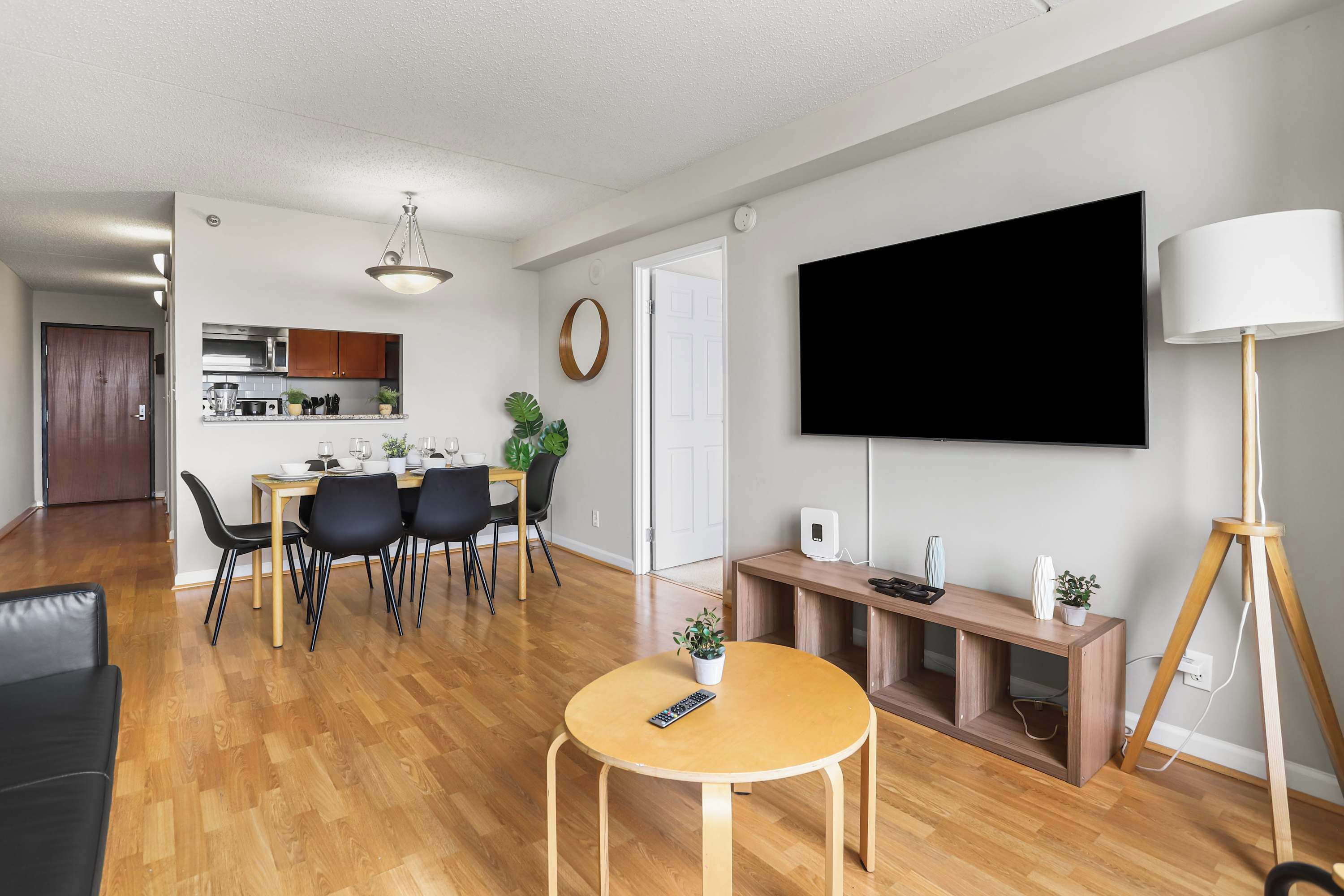 A modern living room with a flat-screen TV, a dining area with chairs and a table, and a kitchen in the background.
