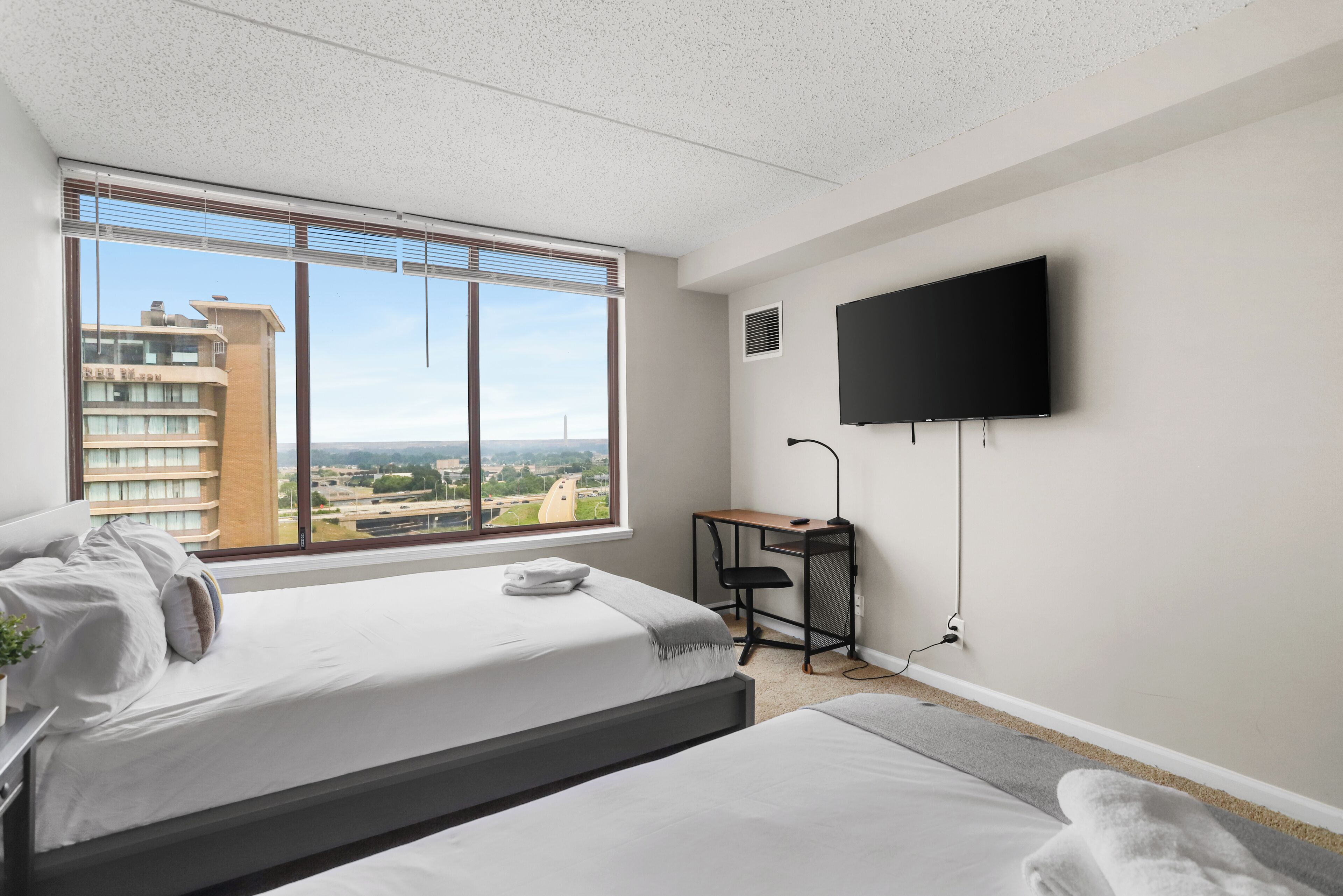 Een hotelkamer met een bed, een bureau, een televisie en uitzicht op een stadsgezicht.