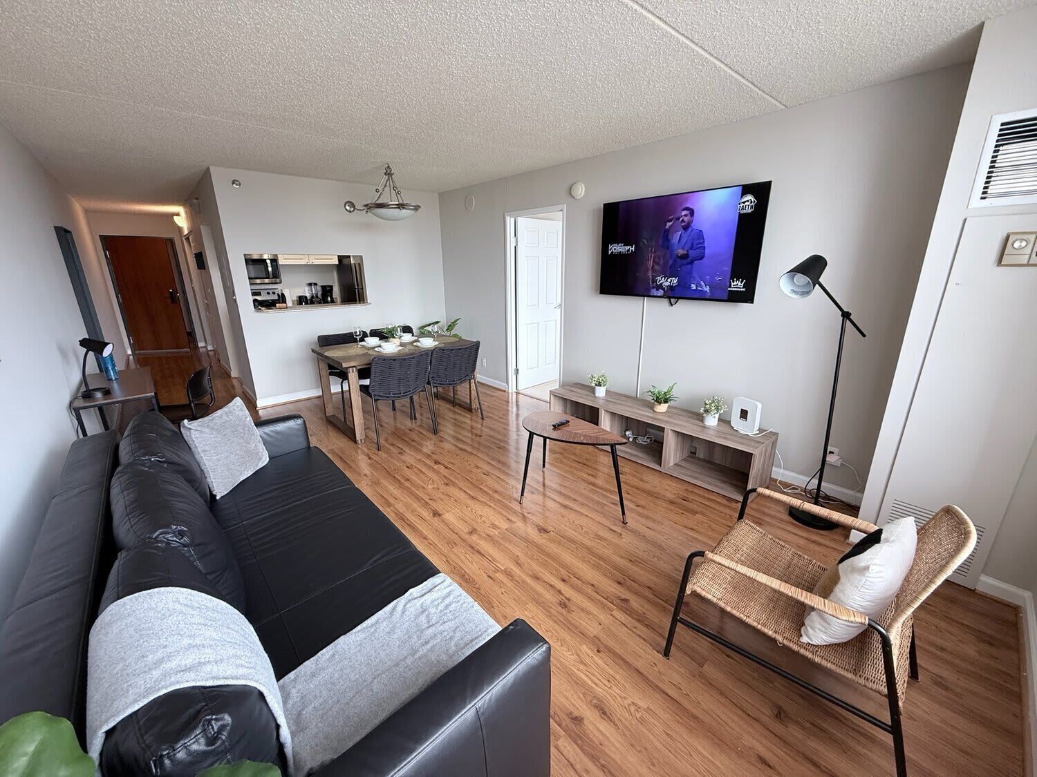 Een moderne woonkamer met een zwarte bank, eettafel en een aan de muur bevestigde televisie.