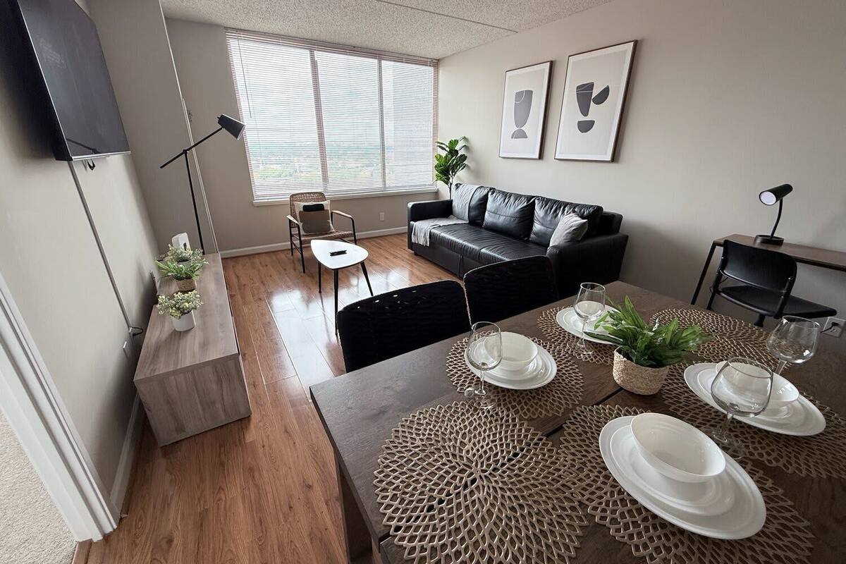 A modern living room with a sofa, dining table set, and a window with blinds.