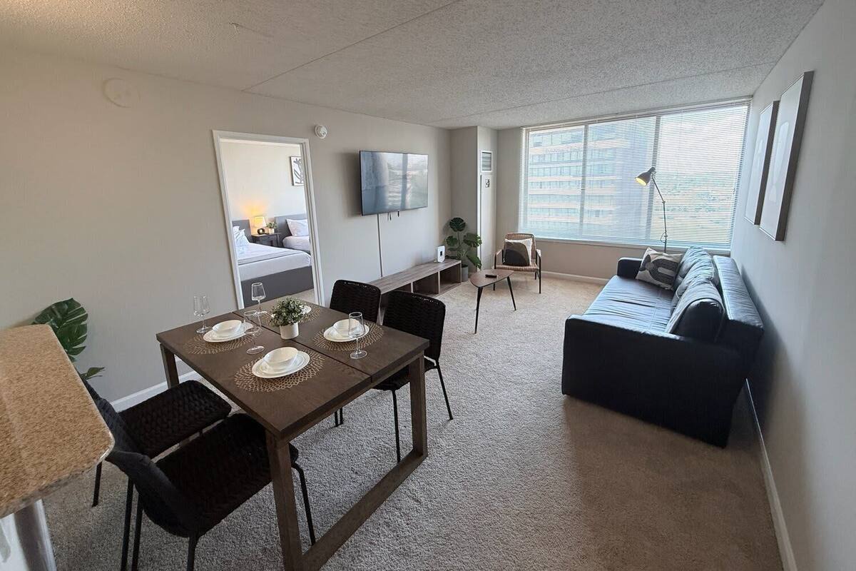 A modern living room with a dining table, sofa, TV, and large windows.
