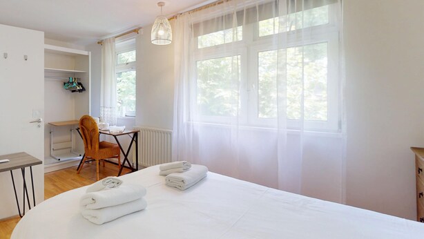 Une chambre à coucher avec un grand lit, un bureau, une chaise et une fenêtre avec des rideaux.