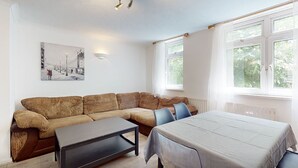 Une pièce comprenant un canapé, une petite table, un lit, une fenêtre et un tableau accroché au mur.