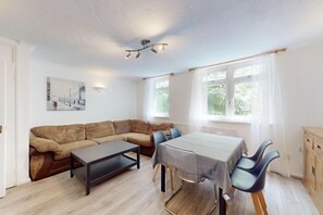 A modern living room with a sofa, a coffee table, a dining table with chairs, and a painting on the wall. - 3BR Home Near Thames-Easy Access to Canary Wharf (London)