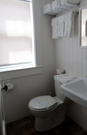 A small bathroom with a toilet, a sink, a window, and a towel rack. - Seaside Escape with Coastal Vibes in North Truro, Massachusetts (North Truro)