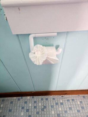 A bathroom with a toilet, a white paper towel holder, and a tiled floor. - Seaside Escape with Coastal Vibes in North Truro, Massachusetts (North Truro)