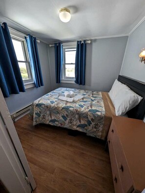 A bedroom with a bed, a dresser, a window with curtains, and a ceiling light. - Seaside Escape with Coastal Vibes in North Truro, Massachusetts (North Truro)