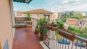 Ein Balkon mit einem Holztisch und Stühlen, Blumentöpfen und Blick auf benachbarte Häuser.