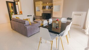 A modern living room with a sofa, dining table, chairs, and a TV. - Expo Smart Living - Two Bedroom Apartment, Sleeps 6 (Verona)