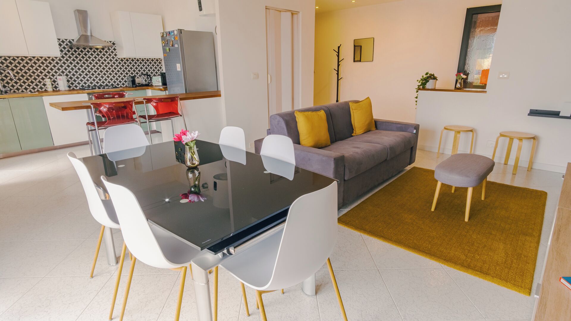 A modern living space with a dining area, sofa, and kitchen.