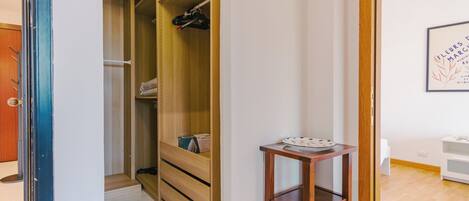 A room with a wooden wardrobe, a small table with a plate, and a framed picture on the wall.