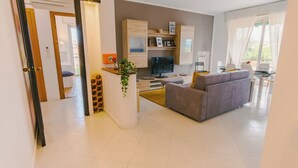 Ein modernes Wohnzimmer mit einem grauen Sofa, einem Fernseher und einem Essbereich mit Tisch und Stühlen.
