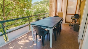 Ein Balkon mit Tisch, Stühlen, Geländer und Blick auf Bäume und Gebäude.